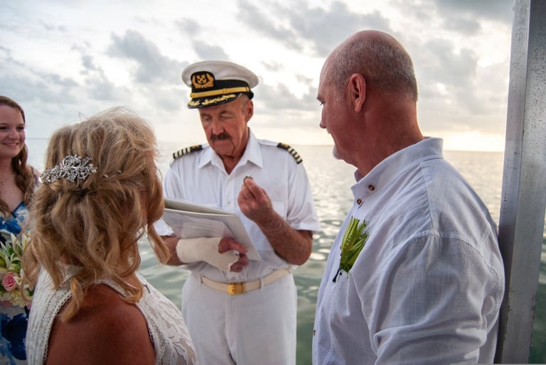 Naval officer in white uniform conducting ceremony with couple on deck overlooking ocean