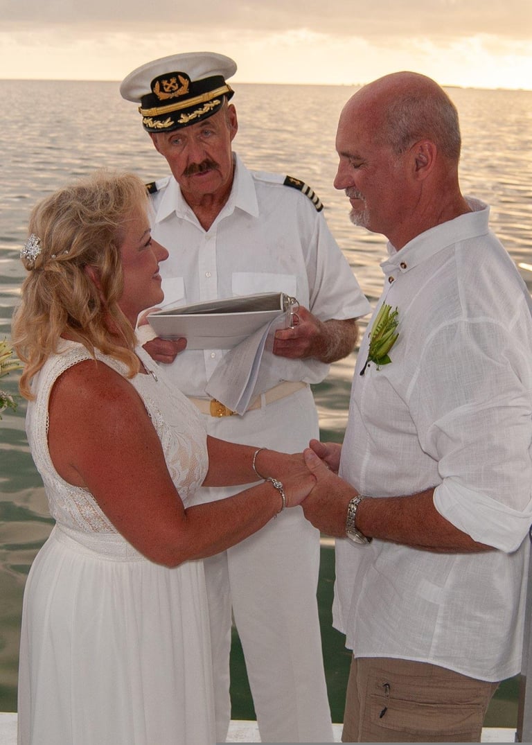 Ship captain performs wedding ceremony for couple in white attire on deck with ocean background